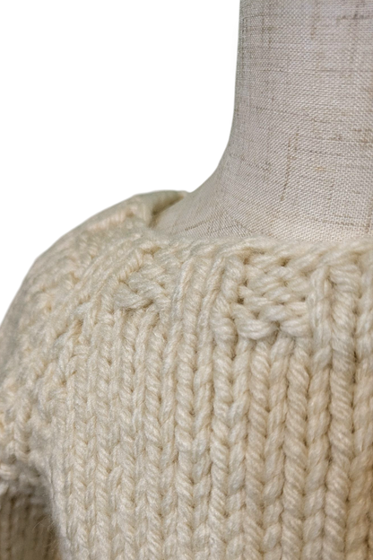 Close-up of a chunky knit sweater in a warm cream or off-white color, displayed on a linen mannequin torso against a white background.