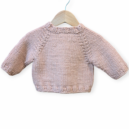 A small hand-knit baby sweater in a soft dusty pink color, hanging on a wooden hanger against a plain white background.