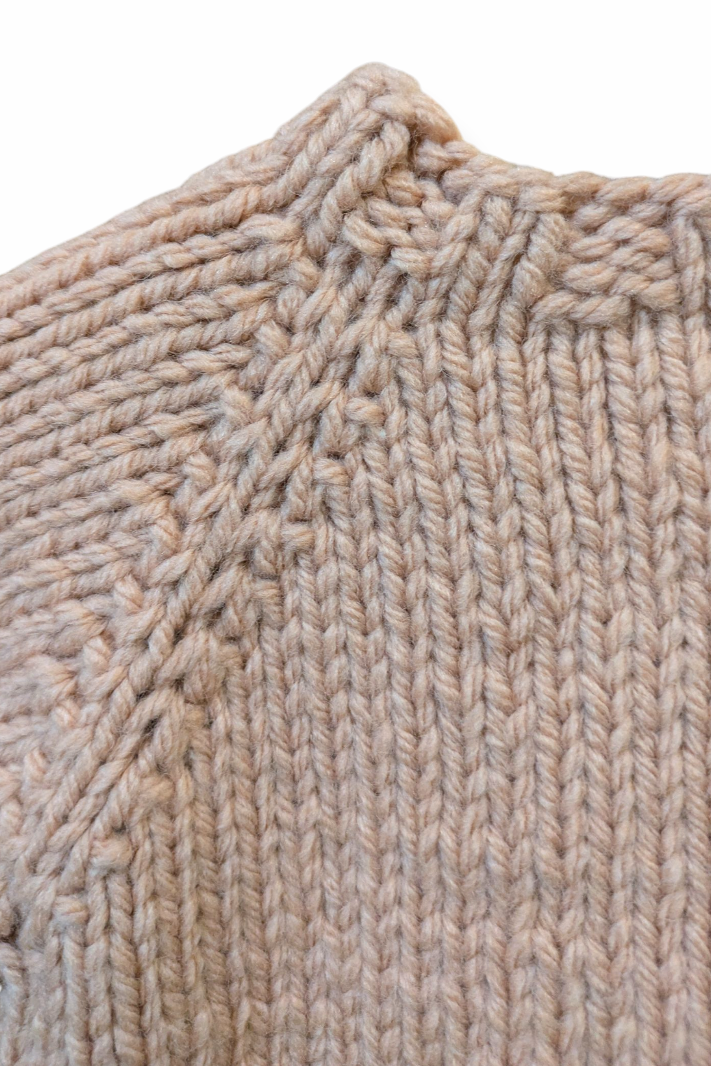 Close-up of a chunky knit sweater in a dusty pink color, showing the neckline and raglan seam details against a plain white background.