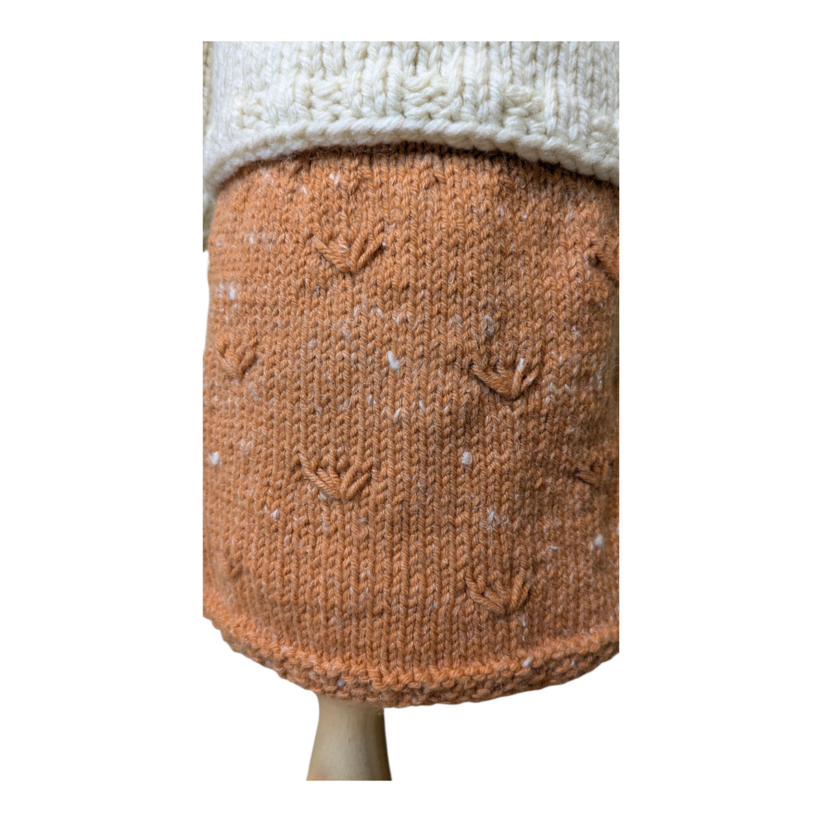 A close-up of a knitted skirt showing a textured muted orange body, displayed on a neutral stand against a white background.